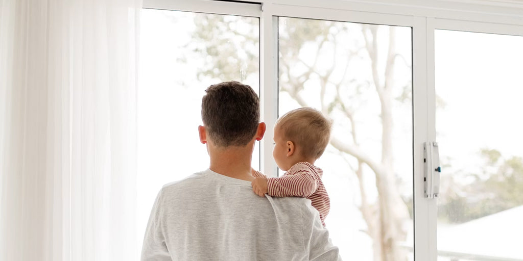 a father hugs his baby standing beside the window