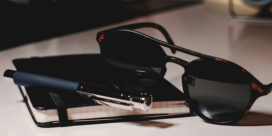 a pen, a glasses and a notebook on a desk
