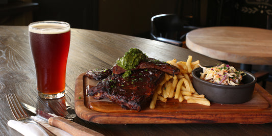 a cut of beer and well grilled steaks on a wood plate to show their good paring