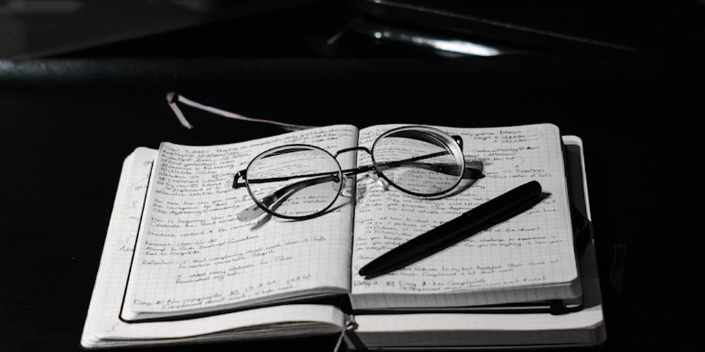 glasses, pen above a notebook with writing