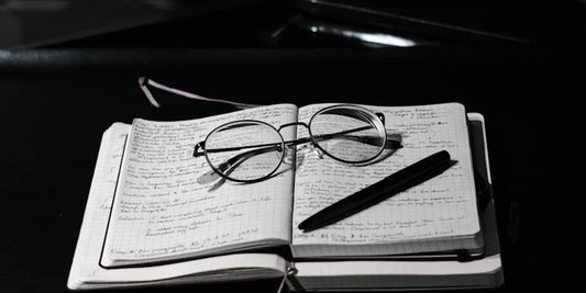 glasses, pen above a notebook with writing
