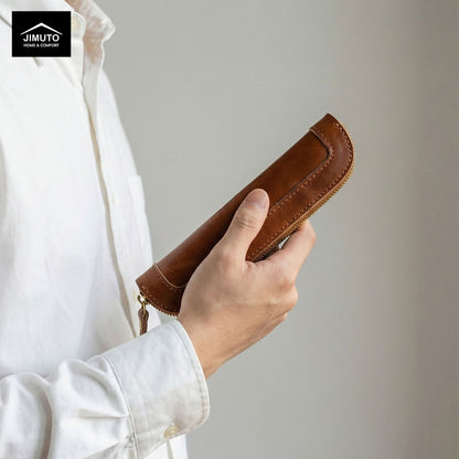 Person holding a brown leather pen case with a plain background