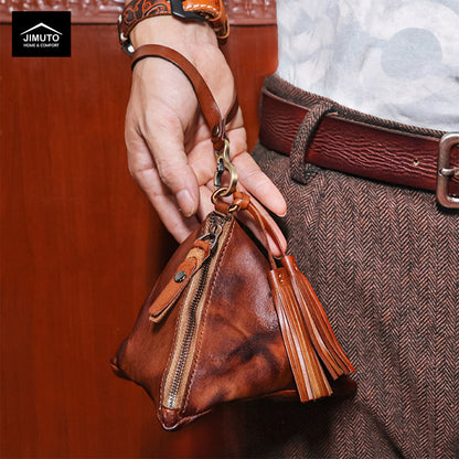 Brown leather handbag with tassel held by a hand, with a blurred background