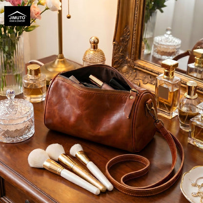 Brown cosmetic and storage leather bag with makeup brushes and perfume bottles on a wooden surface.