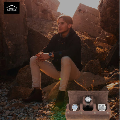Man sitting on rocks with a watch in hand, next to an open watch case displaying three watches.