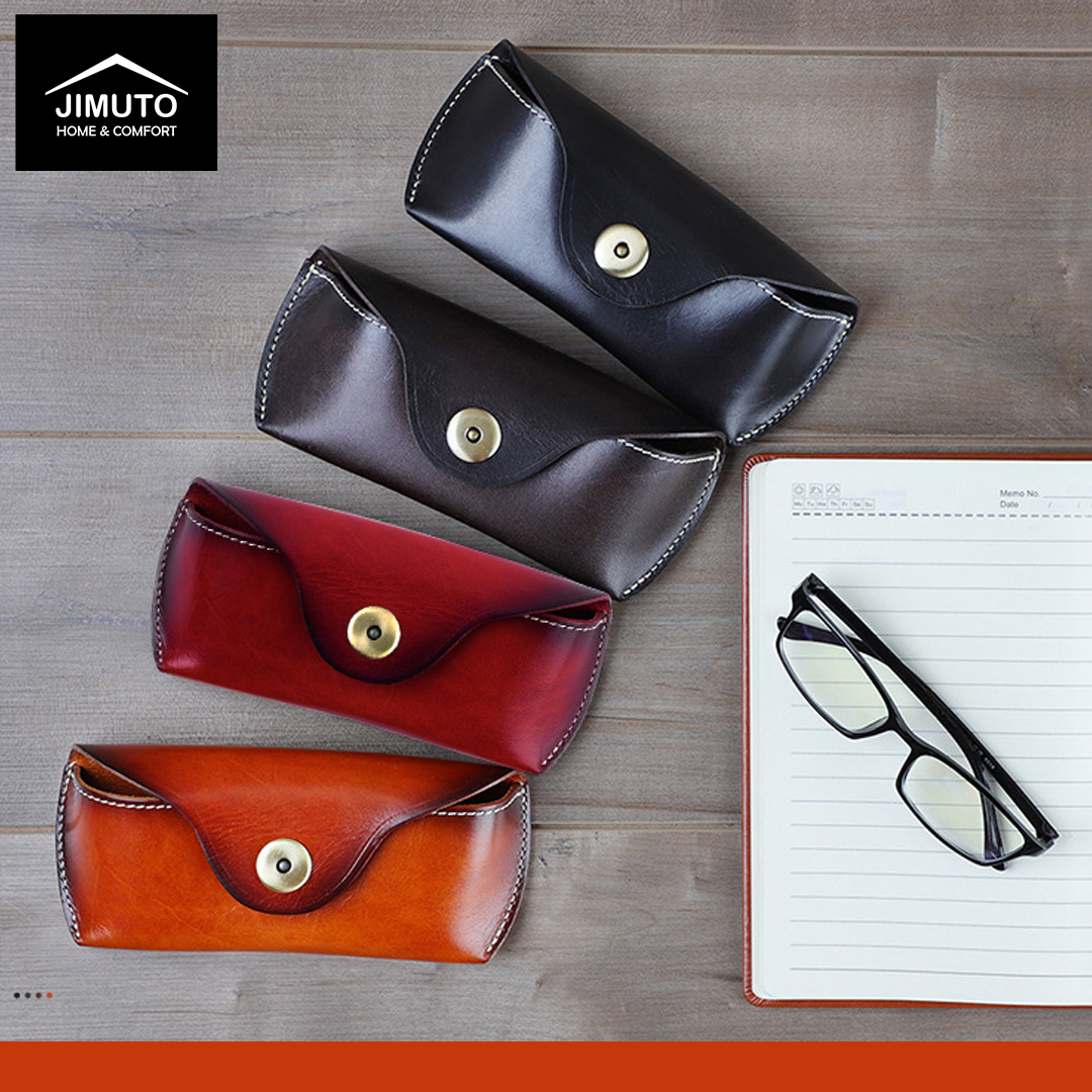 Four leather eyeglass cases in black, brown, red, and orange on a wooden surface with a notebook and glasses.