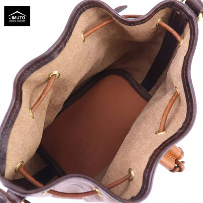 Close-up of the interior of a brown leather bucket bag, showing a tan suede-like lining, tan leather drawstrings with gold-tone metal eyelets, and a brown leather base. A black Jimuto logo is visible in the top-left corner.