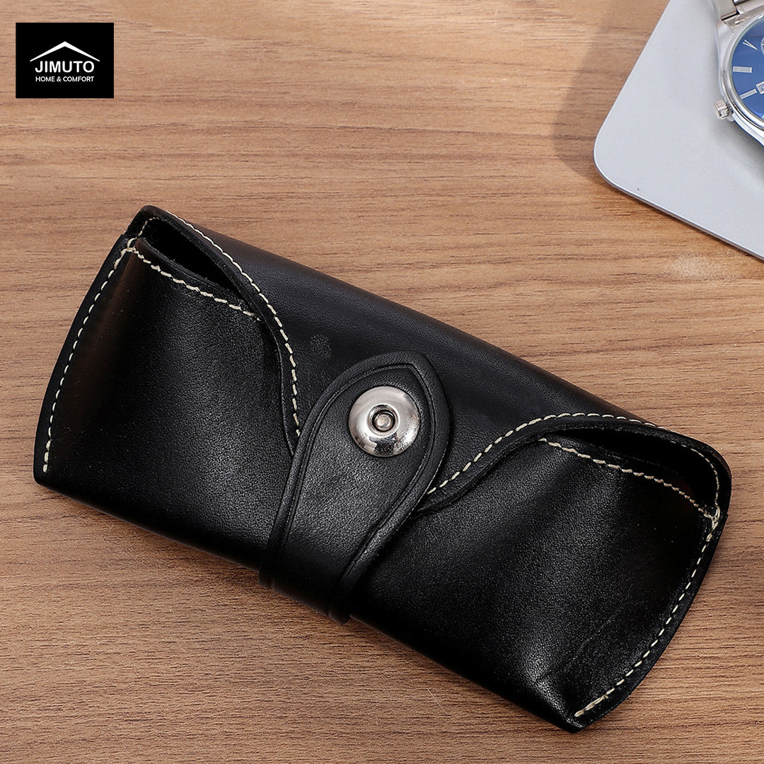 A black leather eyewear case with white contrast stitching and a silver snap button, shown on a wooden desk with a Jimuto logo in the top-left corner.