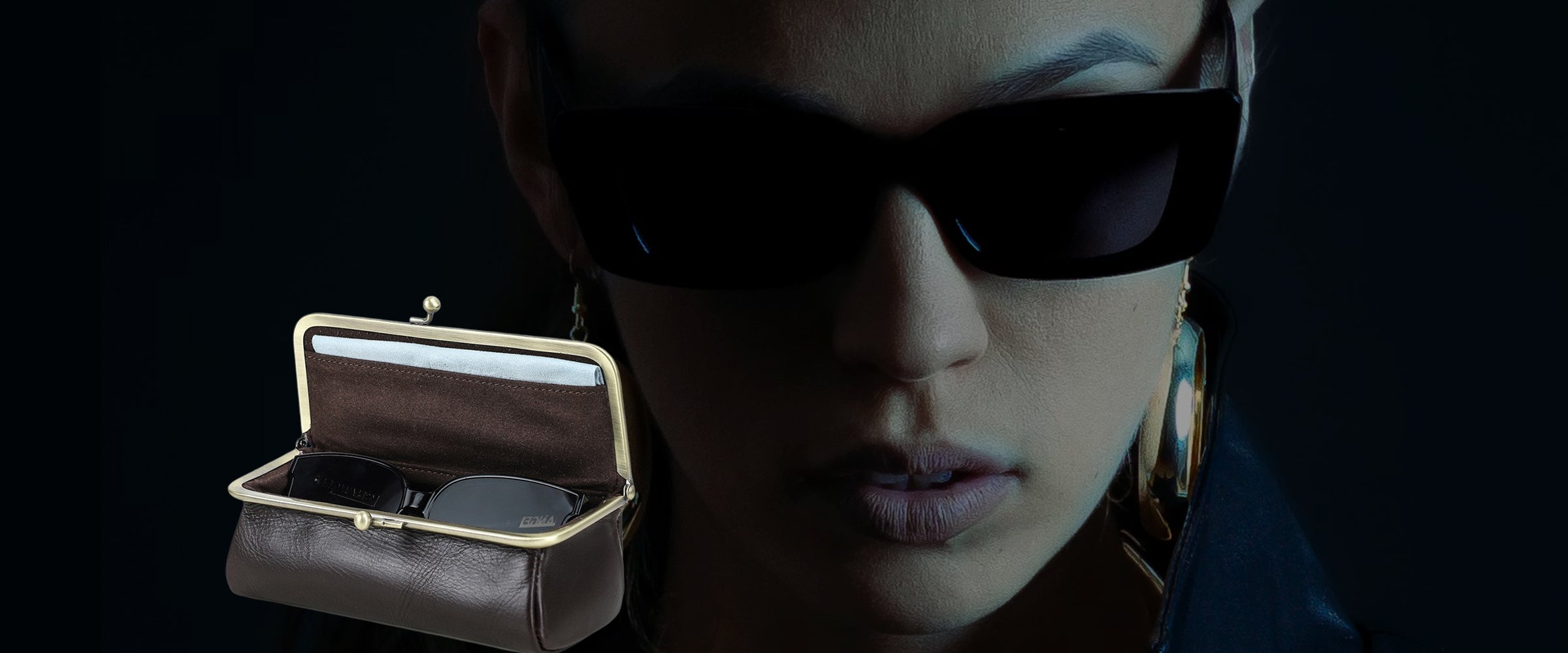 Person wearing sunglasses with a small open leather sunglasses box in the foreground on a dark background