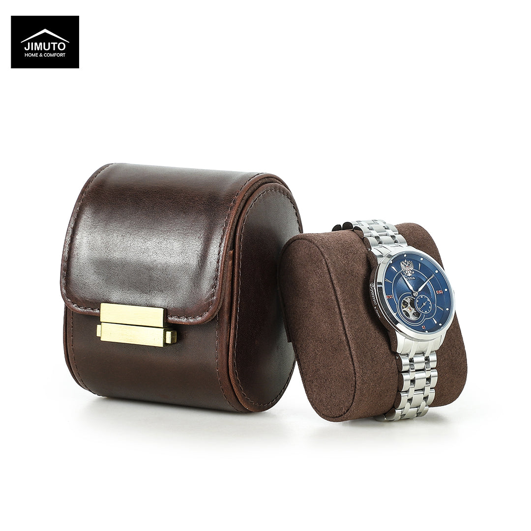 A dark brown full-grain leather watch box with a gold-tone clasp next to a matching brown suede watch cushion holding a silver metal bracelet watch with a blue dial. The Jimuto brand logo is visible in the top-left corner.