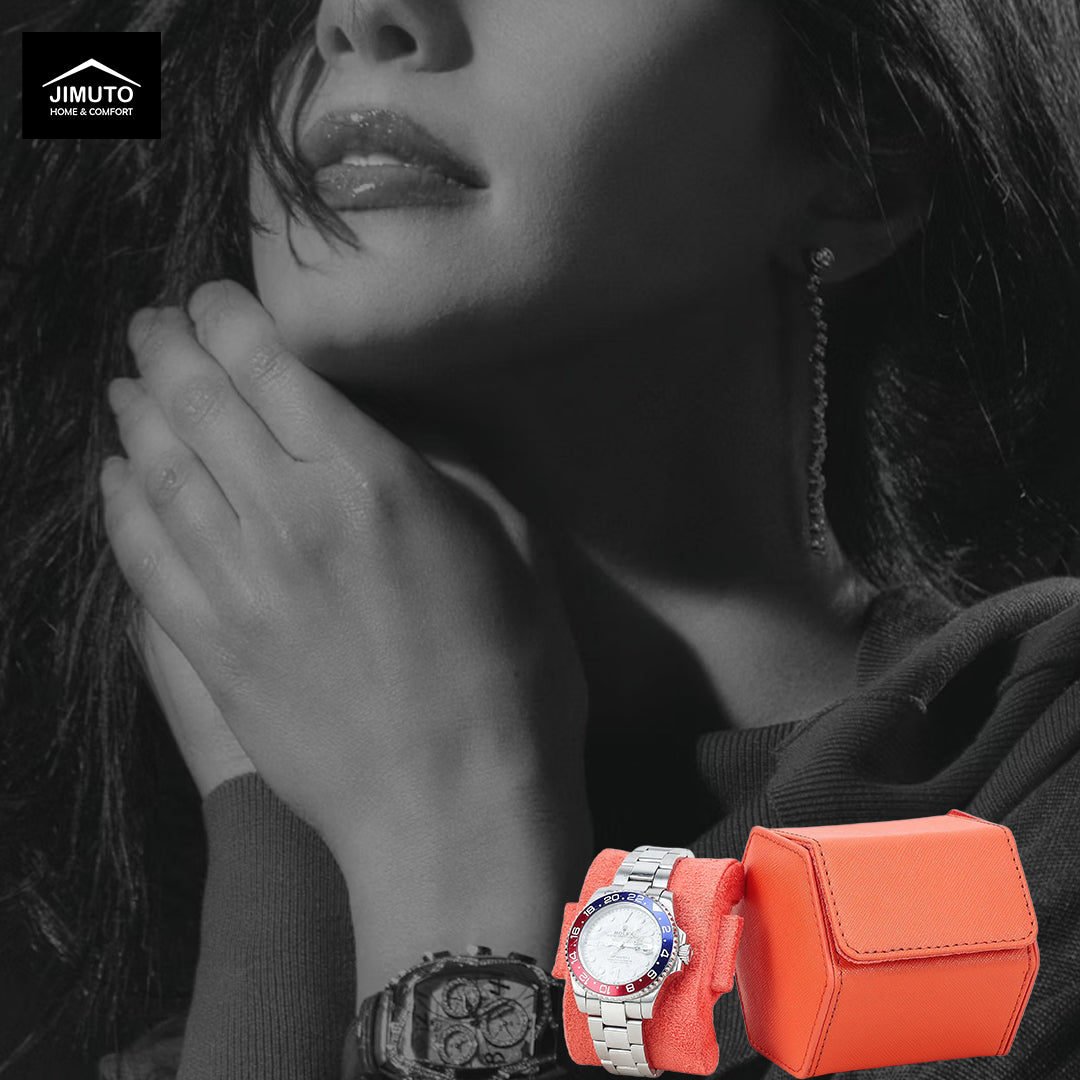A close-up lifestyle shot of a woman wearing a silver-toned watch with a bright orange strap and a matching orange leather watch case. The background is desaturated black and white, with the model's face, hands, and hair rendered in grayscale.