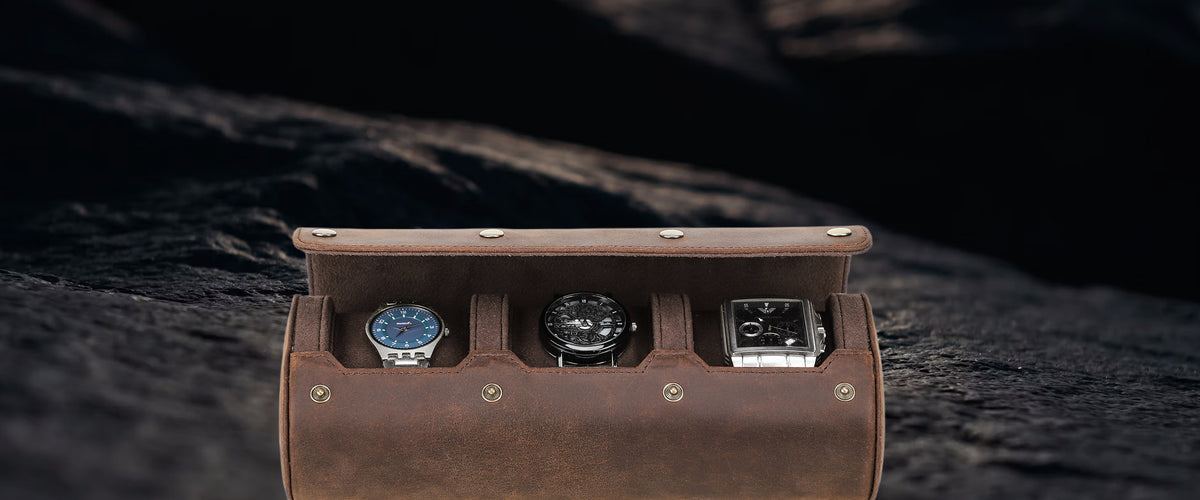 A brown crazy horse leather watch storage case with three compartments, shown open with three watches inside, set against a dark textured rock background.