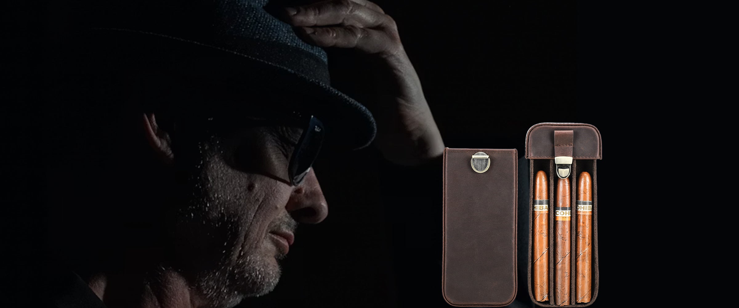 A man in profile wearing a dark fedora and sunglasses, with a small brown leather cigar case and three cigars displayed on a black background.